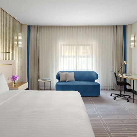 Radisson Blu Plaza Hotel Sydney Zewnętrze zdjęcie The photo shows a modern hotel room featuring a large bed with white linens. There's a small table with a flower vase next to the bed. A blue sofa is positioned against one wall, and a desk with a chair is situated nearby. The room has soft, diffused