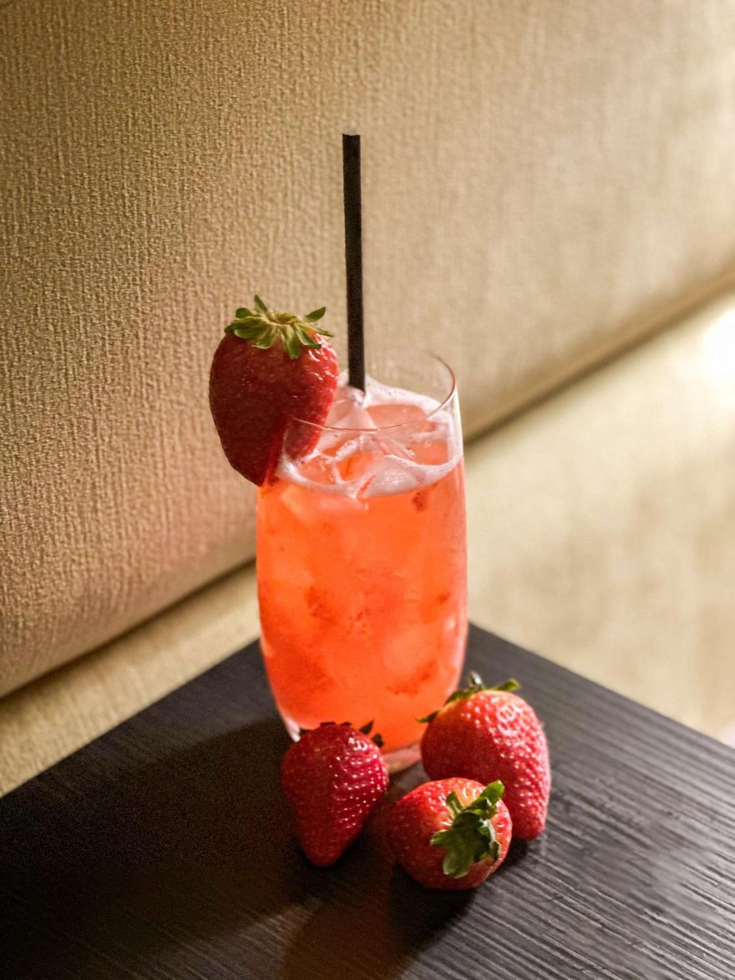 Radisson Blu Plaza Hotel Sydney Zewnętrze zdjęcie The photo shows a refreshing beverage in a tall glass. The drink is a vibrant pink color and appears to be served over ice. It has a black straw inserted into it. Adorning the glass are fresh strawberries on the rim, complementing the drink. Addition