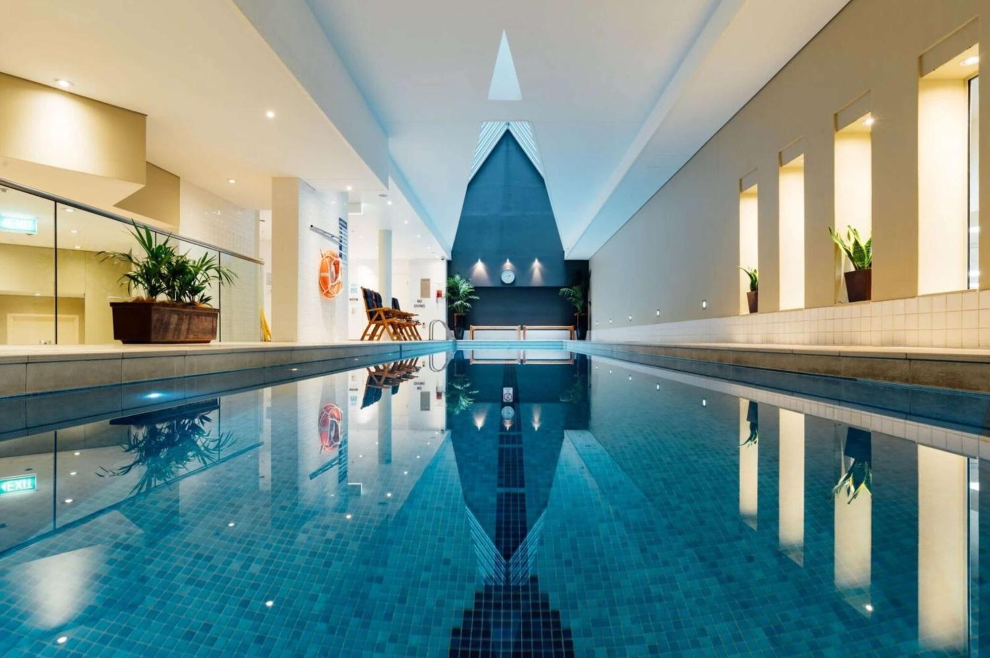 Radisson Blu Plaza Hotel Sydney Zewnętrze zdjęcie The photo shows an indoor swimming pool in a modern, well-lit space. The pool has clear blue water and reflects the light from the surroundings. The architecture features a high ceiling and a triangular design element at one end of the pool. There ar