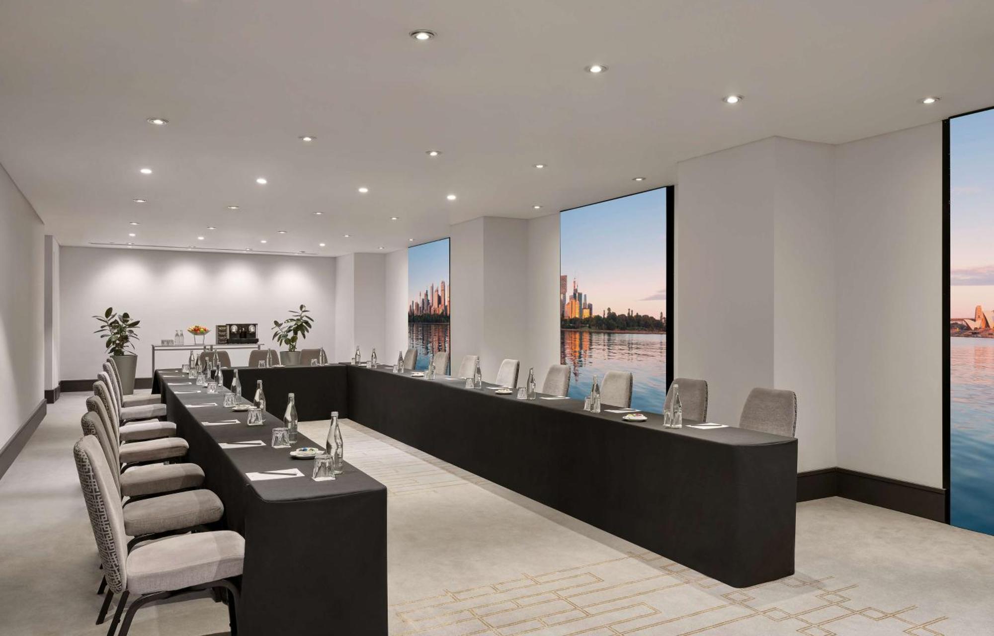 Radisson Blu Plaza Hotel Sydney Zewnętrze zdjęcie The photo depicts a modern conference room set up for a meeting. The room features a long, rectangular table with multiple chairs arranged along its sides. Each chair is equipped with items such as water bottles and notepads. Large windows allow natu